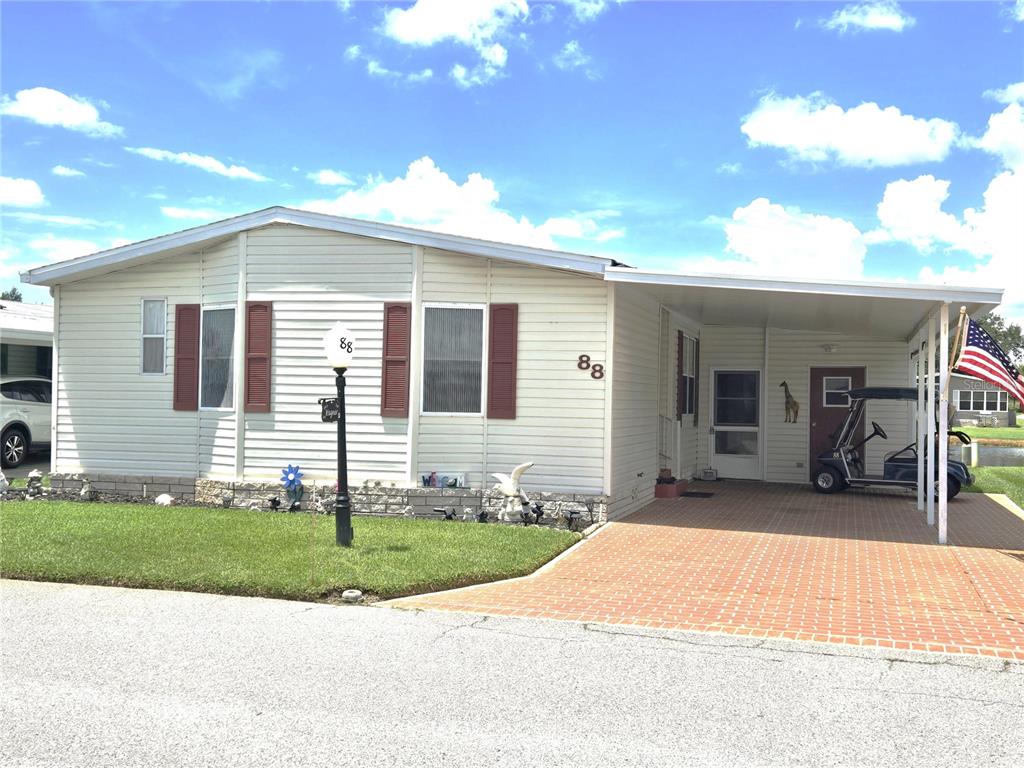 A single-story mobile home with light siding, red shutters, and a brick-paved carport — 88 STRAPHMORE DRIVE, HAINES CITY, FL