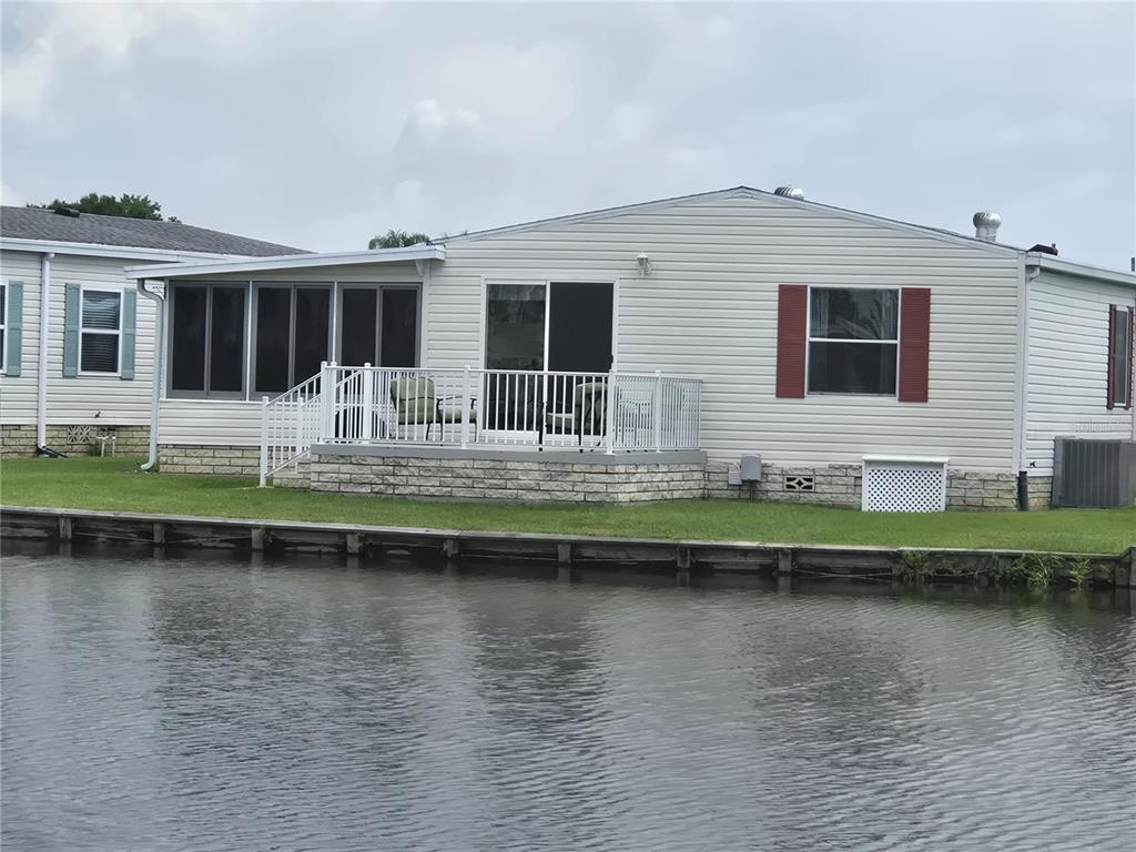 A waterfront mobile home features a screened-in porch, a deck with white railings, and siding — 88 STRAPHMORE DRIVE, HAINES CITY, FL