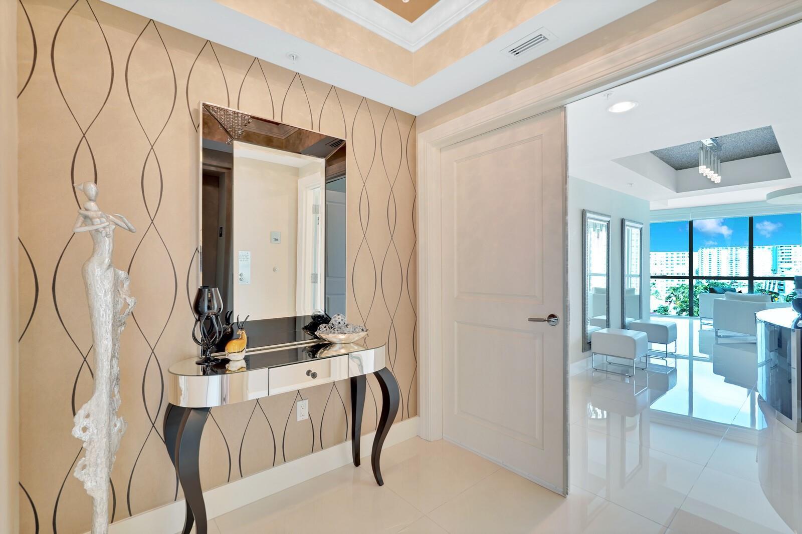 A foyer features patterned wallpaper, a mirrored console table, and a doorway leading to a living area — 1 N Ocean Boulevard # 607, Pompano Beach FL 33062, POMPANO BEACH, FL