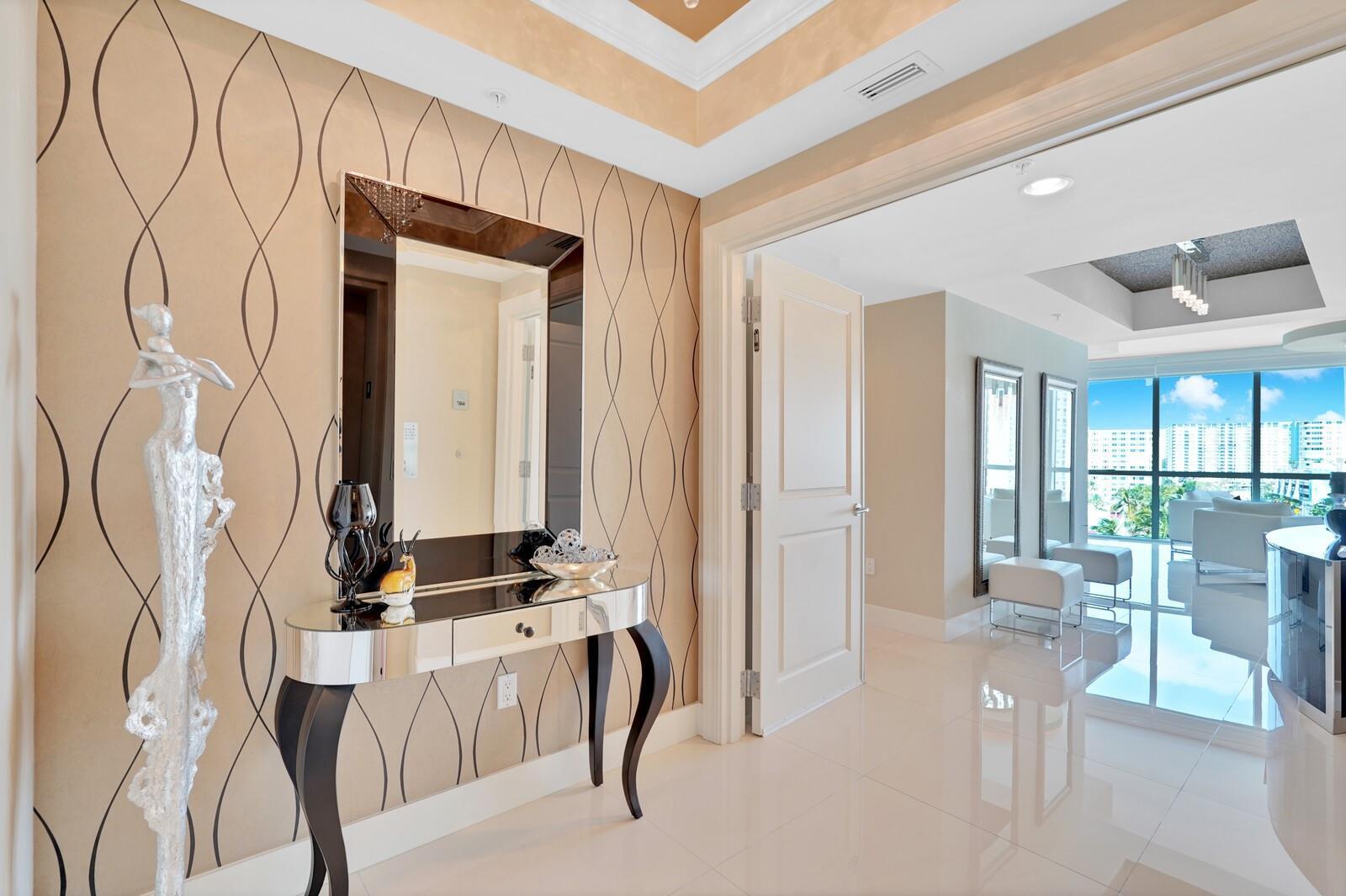 An entryway features a mirrored console table, a wall mirror, and patterned wallpaper — 1 N Ocean Boulevard # 607, Pompano Beach FL 33062, POMPANO BEACH, FL