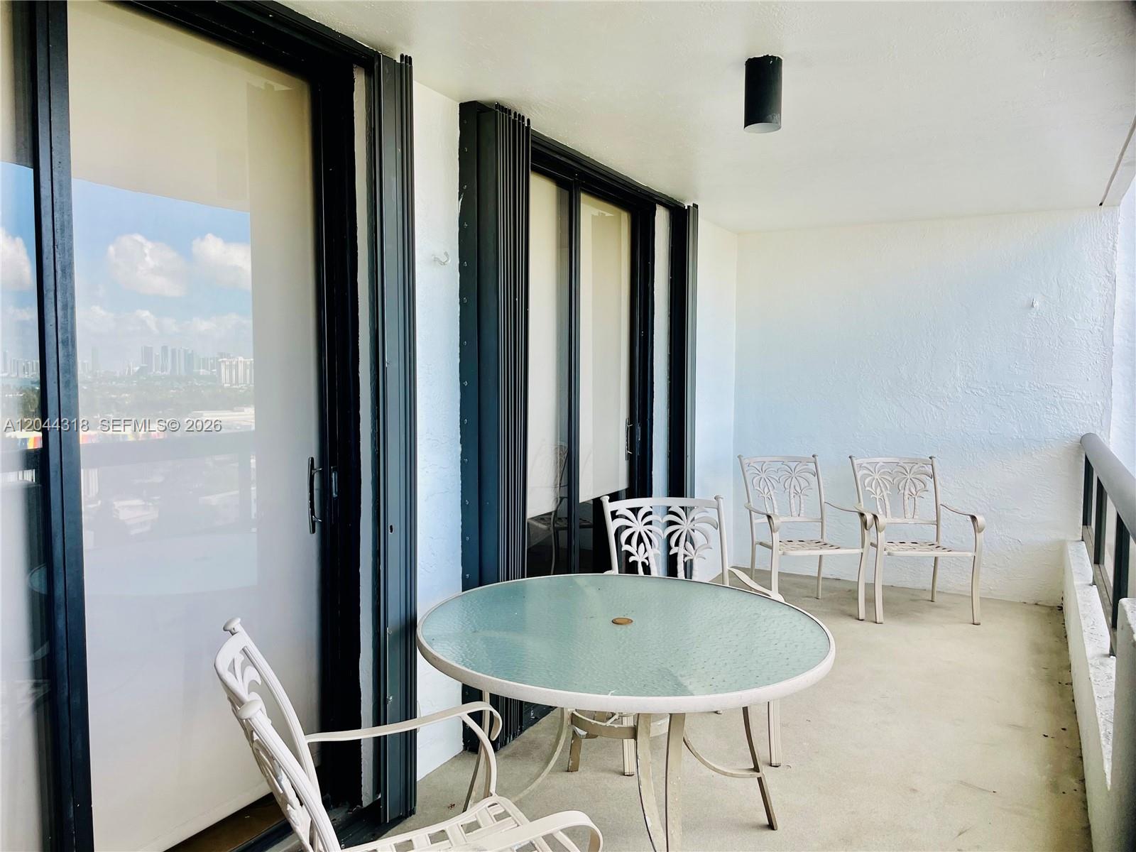 A balcony features a glass-topped table, four metal chairs, and sliding glass doors — 2555 Collins Ave # 2006, Miami Beach FL 33140, MIAMI BEACH, FL