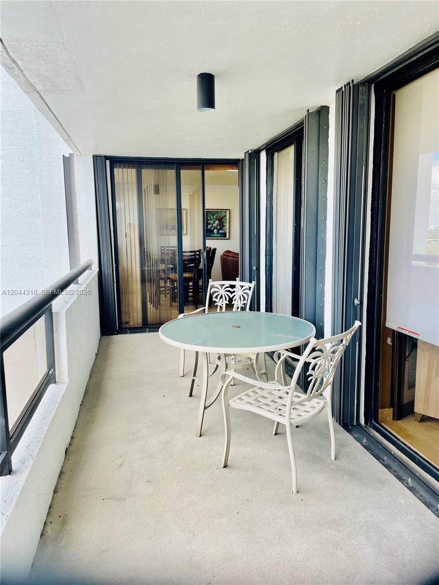 A balcony features a glass-topped table, two white metal chairs, and sliding glass doors — 2555 Collins Ave # 2006, Miami Beach FL 33140, MIAMI BEACH, FL