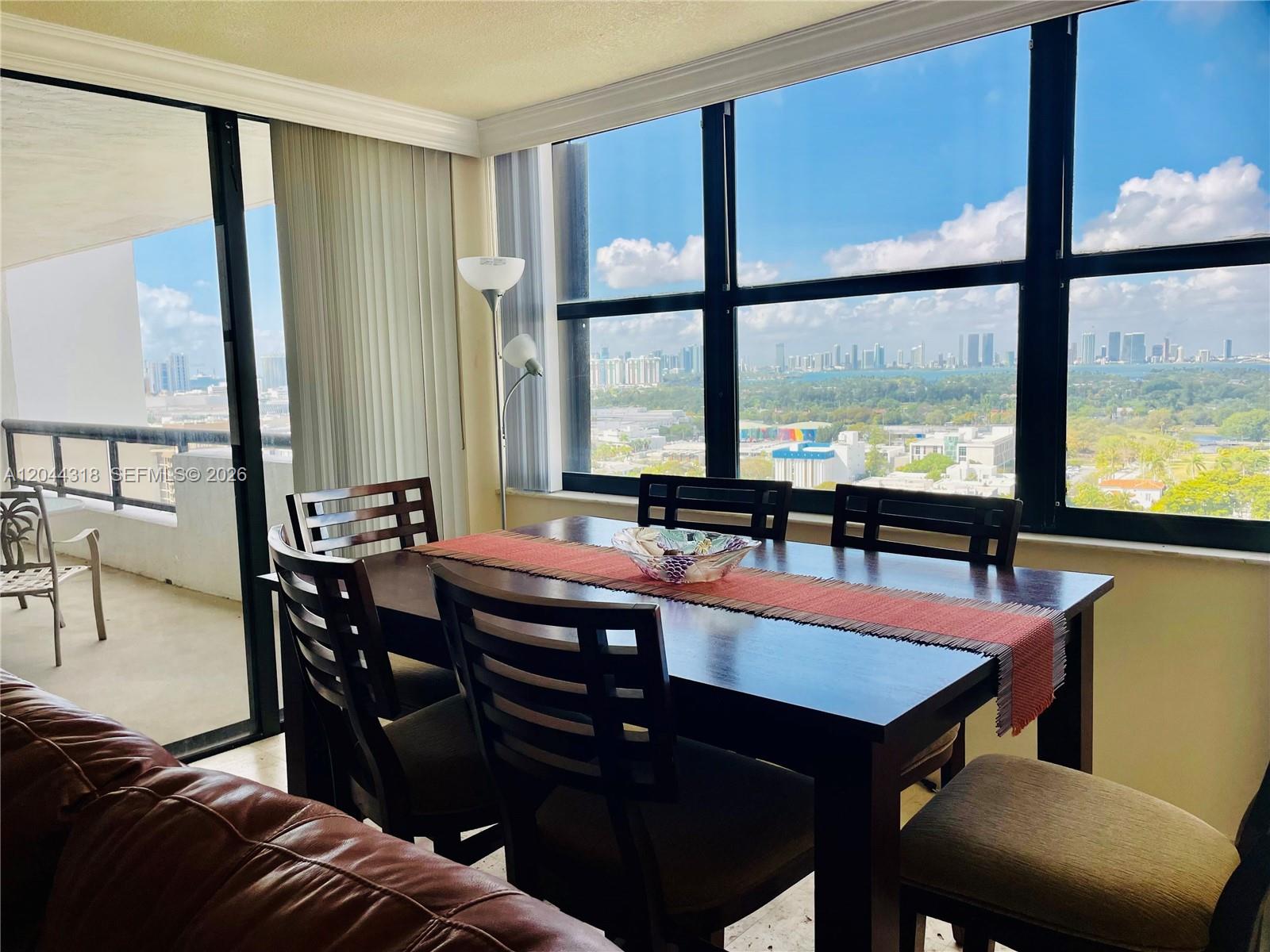 A dining area with a dark wood table and chairs overlooks a city skyline view — 2555 Collins Ave # 2006, Miami Beach FL 33140, MIAMI BEACH, FL