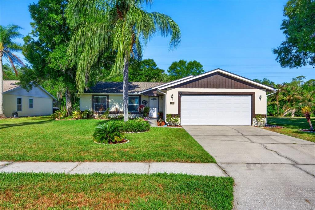 A single-story house with a white garage, brown trim, and a large palm tree — 549 LONGWOOD CIRCLE, OLDSMAR, FL