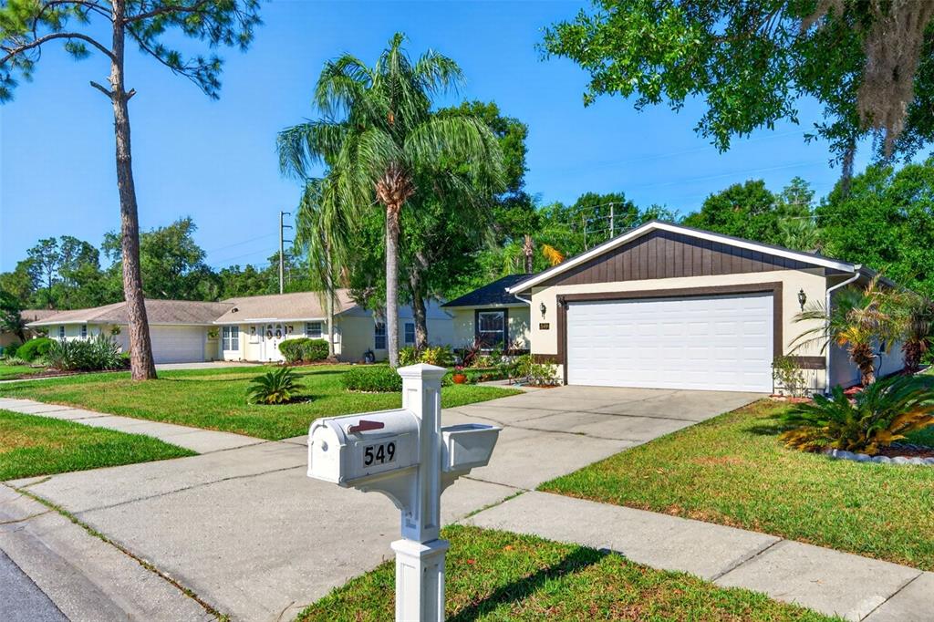 A white mailbox stands in the foreground of a suburban house with a two-car garage — 549 LONGWOOD CIRCLE, OLDSMAR, FL