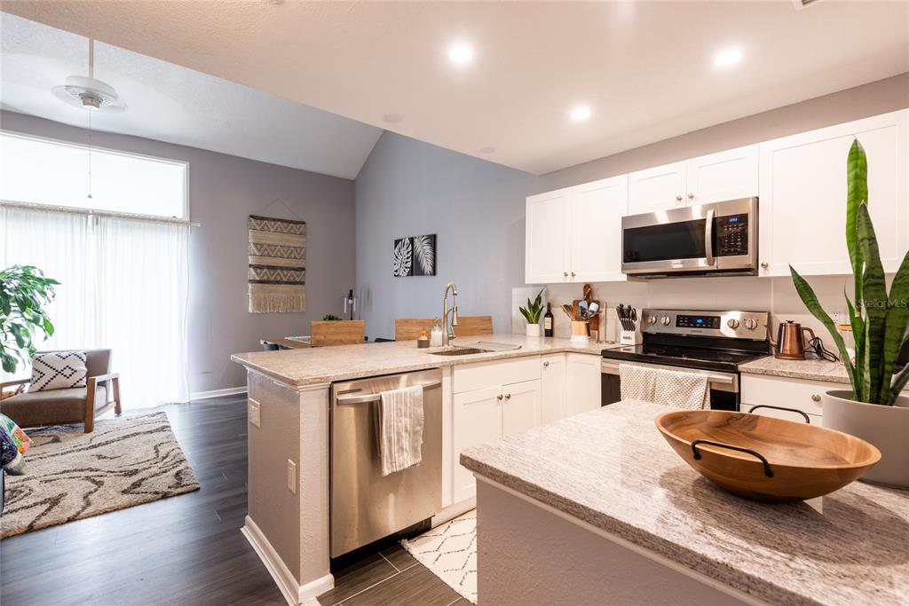 A modern kitchen features white cabinets, granite countertops, stainless steel appliances, and an open layout — 2643 ST JOSEPHS DRIVE W, DUNEDIN, FL