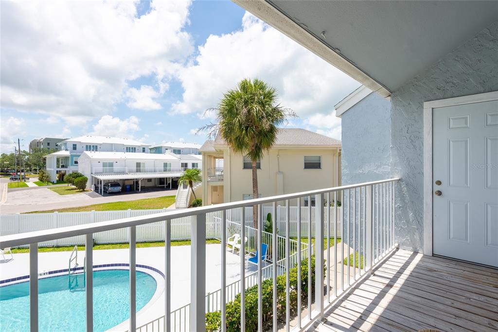 A balcony overlooks a swimming pool, a white fence, and neighboring residential buildings — 2643 ST JOSEPHS DRIVE W, DUNEDIN, FL