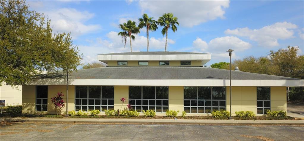 A single-story commercial building with a yellow facade, large windows, and three palm trees behind — 7485 SANDLAKE COMMONS BOULEVARD, ORLANDO, FL