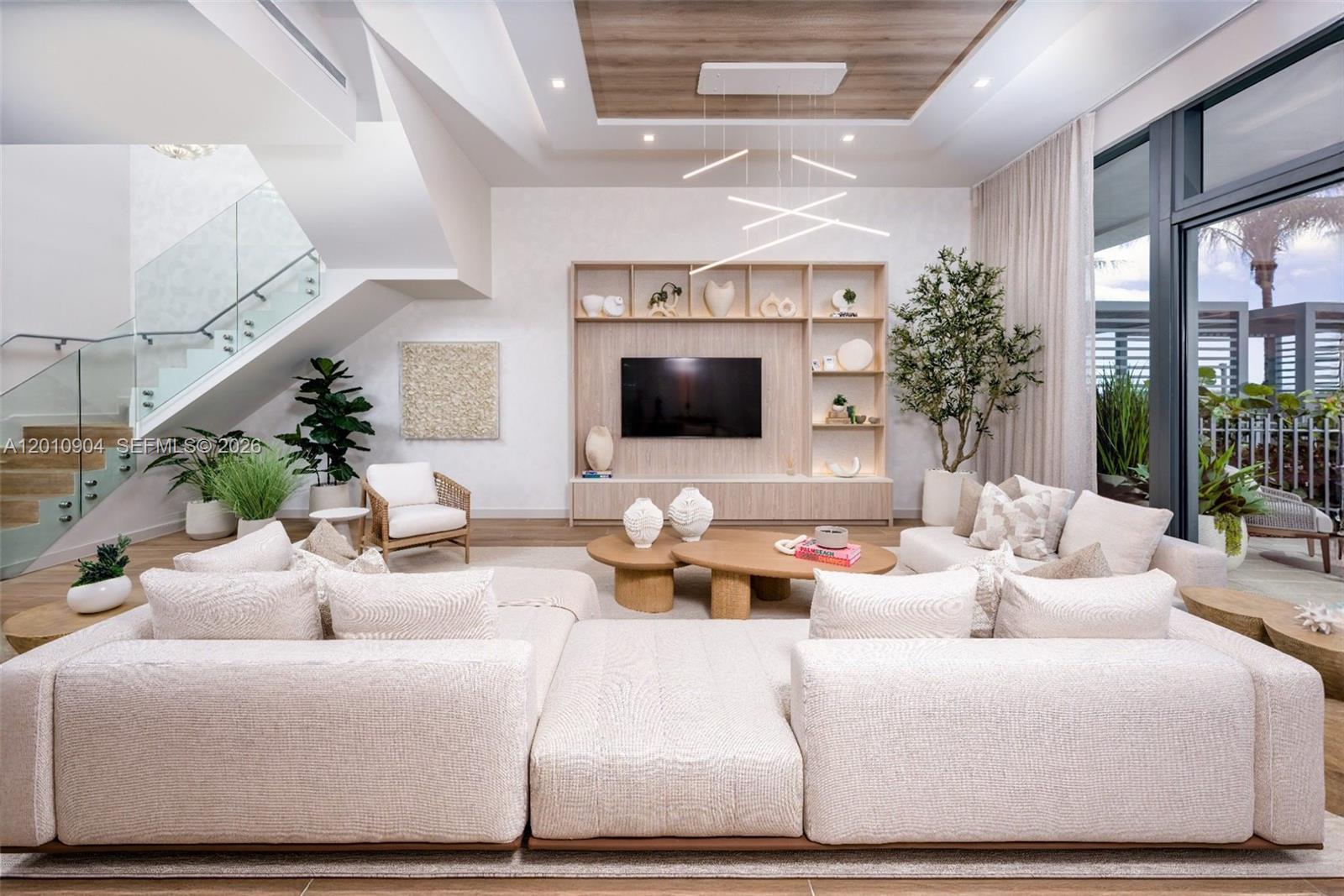 A modern living room features a large sectional sofa, built-in shelving, and a floating staircase — 900 N Ocean Blvd # 101, Pompano Beach FL 33062, POMPANO BEACH, FL