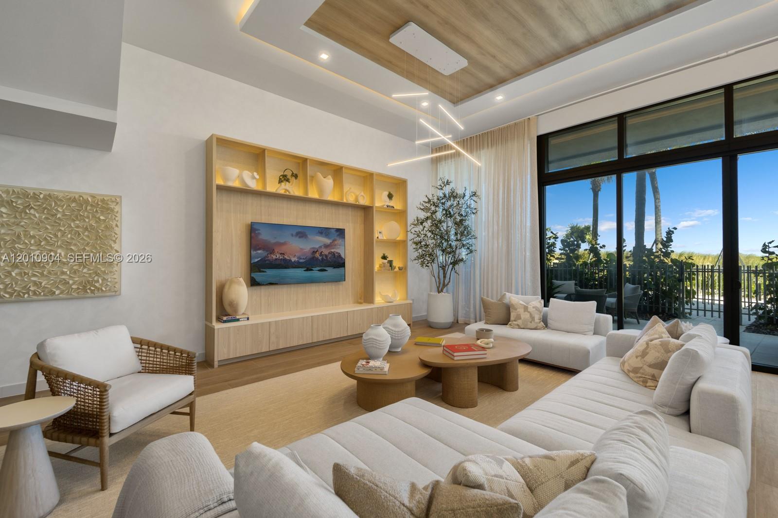 A modern living room features a light wood media wall, sectional sofa, and floor-to-ceiling windows — 900 N Ocean Blvd # 101, Pompano Beach FL 33062, POMPANO BEACH, FL