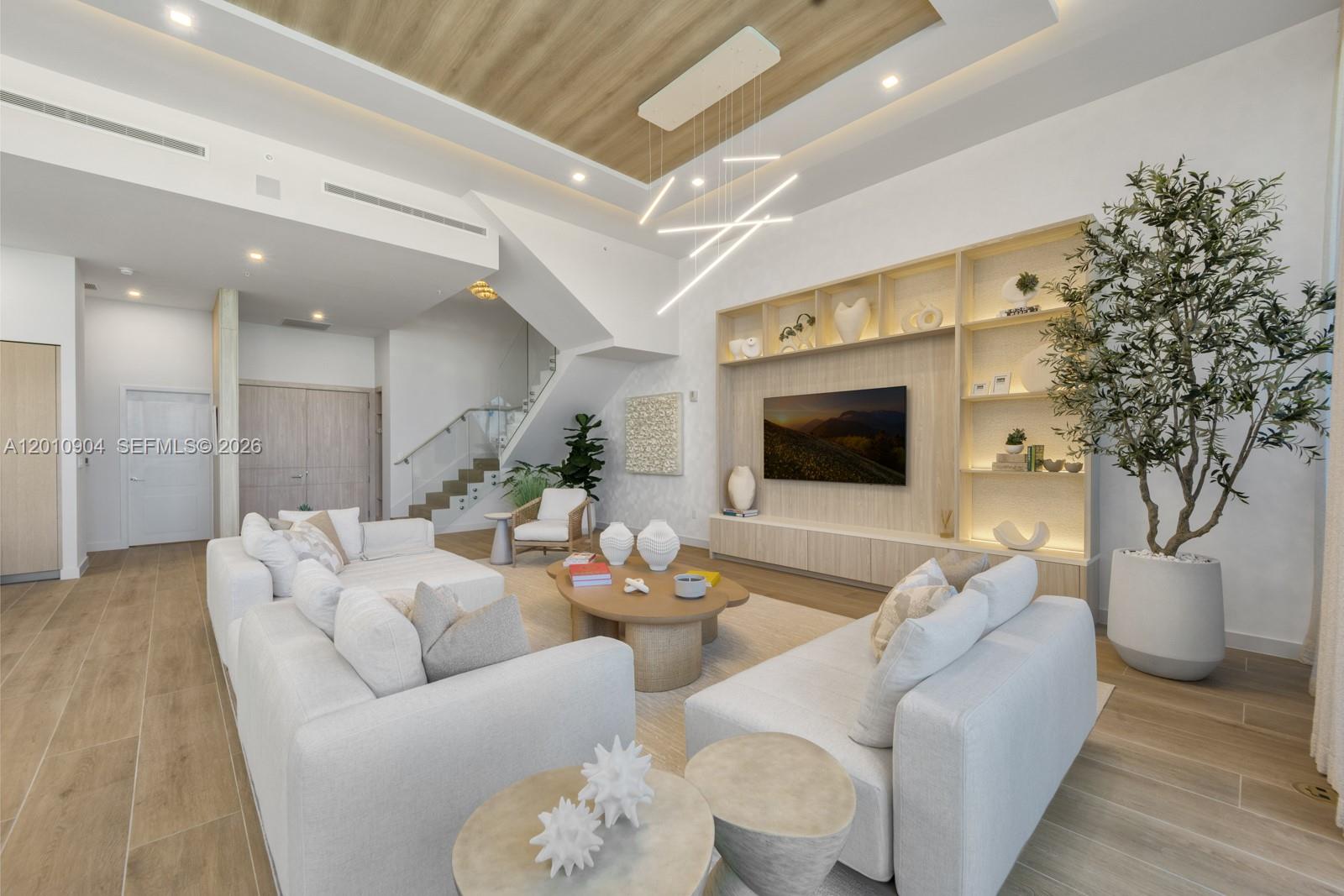 A modern living room features white sofas, a wooden media wall, and a staircase — 900 N Ocean Blvd # 101, Pompano Beach FL 33062, POMPANO BEACH, FL