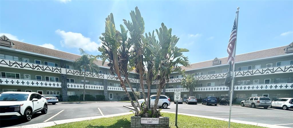 A multi-story apartment complex features a central courtyard with a sign and palm trees — 2447 ECUADORIAN WAY UNIT 73, CLEARWATER, FL