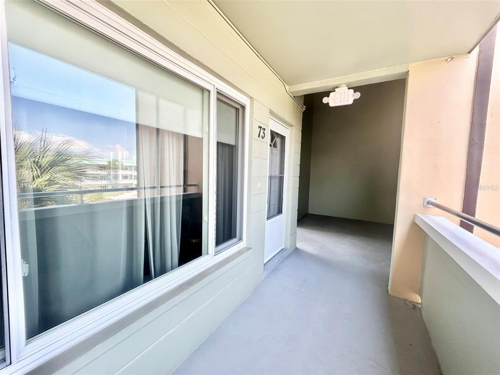 An exterior walkway leads to the entrance of a unit marked with the number 73 — 2447 ECUADORIAN WAY UNIT 73, CLEARWATER, FL