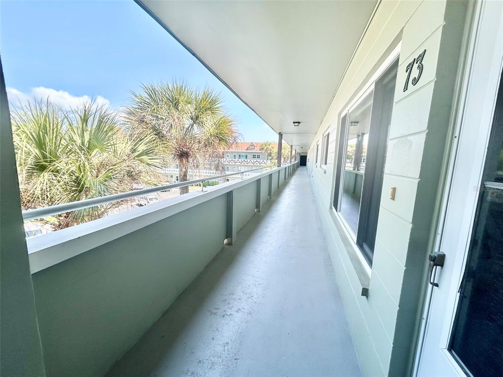 An outdoor walkway with a metal railing overlooks palm trees and a neighboring building — 2447 ECUADORIAN WAY UNIT 73, CLEARWATER, FL