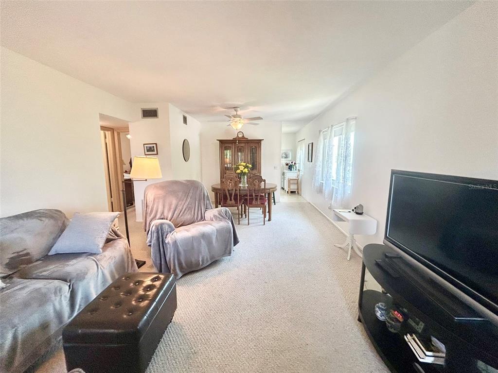 A living room with carpeted floors, a television, and a dining area in the background — 2447 ECUADORIAN WAY UNIT 73, CLEARWATER, FL