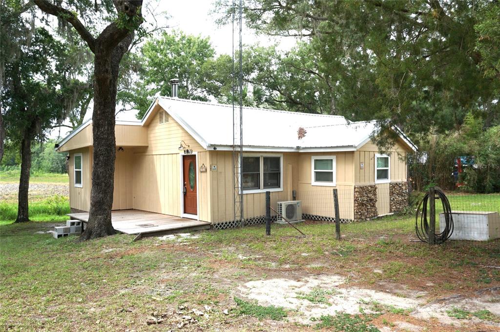 A single-story yellow house with a metal roof and a wooden deck sits among trees — 5470 NE 165TH TERRACE ROAD, SILVER SPRINGS, FL
