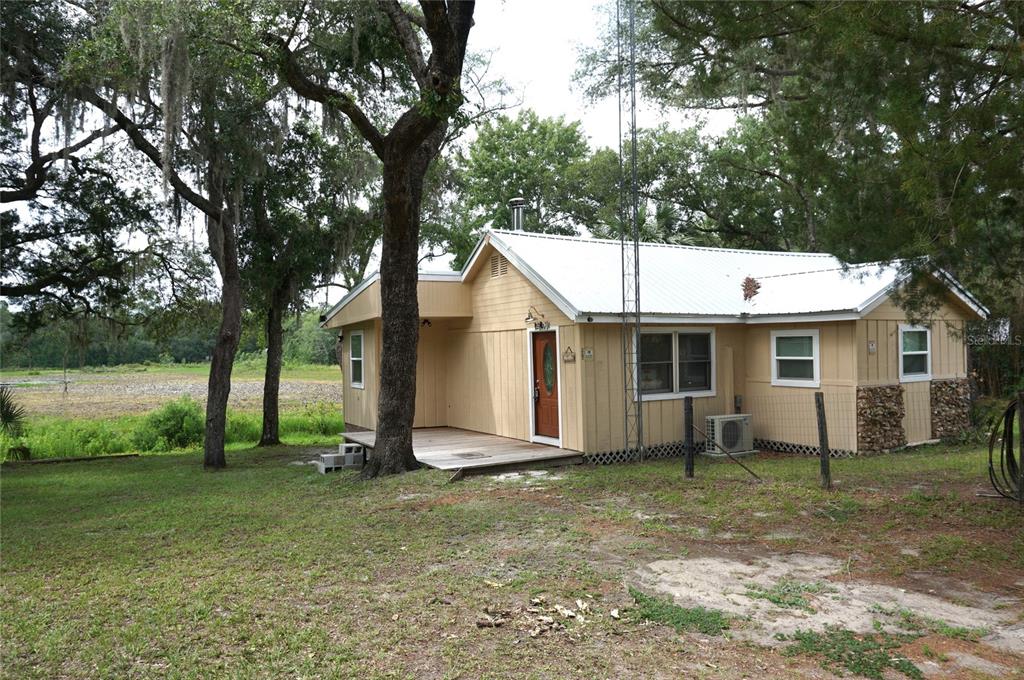 A single-story tan house with a metal roof sits on a grassy lot with trees — 5470 NE 165TH TERRACE ROAD, SILVER SPRINGS, FL