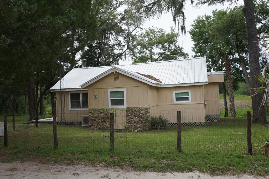 A tan, single-story house with a white metal roof sits behind a wire fence — 5470 NE 165TH TERRACE ROAD, SILVER SPRINGS, FL