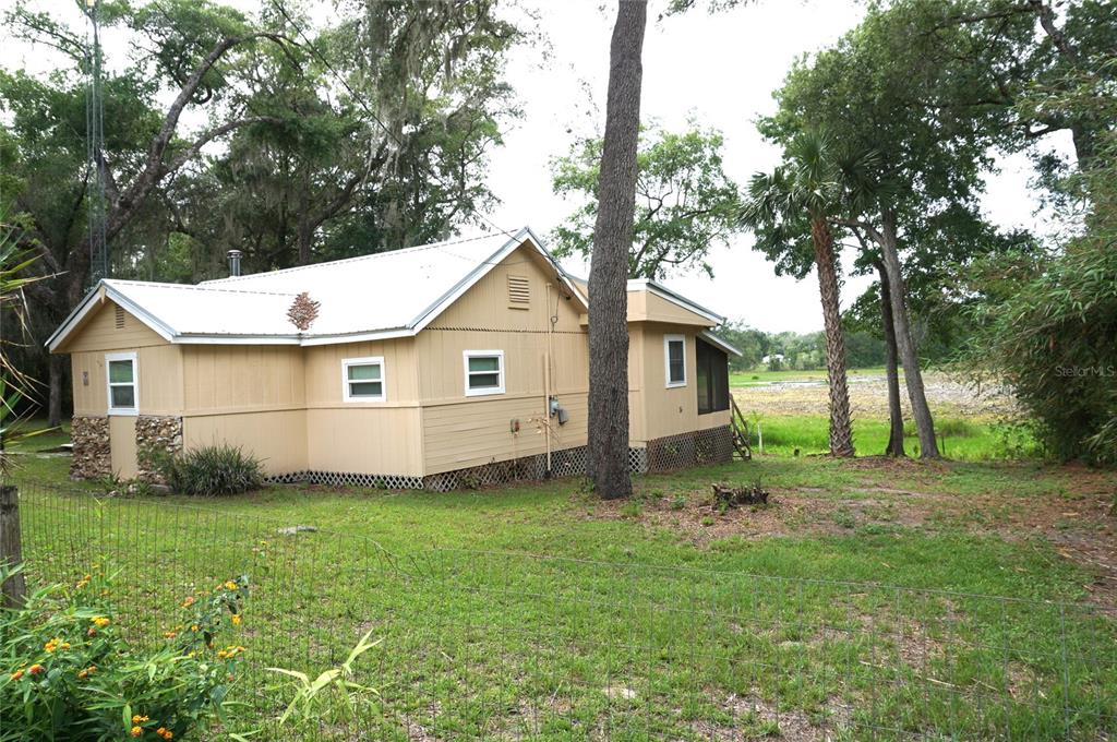 A tan, single-story house with a metal roof sits on a grassy lot with trees — 5470 NE 165TH TERRACE ROAD, SILVER SPRINGS, FL