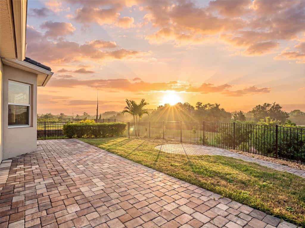 A paved patio overlooks a grassy backyard enclosed by a black metal fence at sunset — 16049 VOLTERRA POINT, MONTVERDE, FL