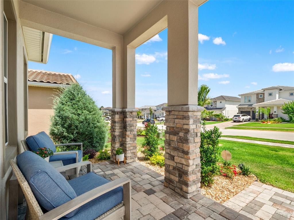 A covered front porch features stone-based columns, paver flooring, and two blue outdoor chairs — 16049 VOLTERRA POINT, MONTVERDE, FL