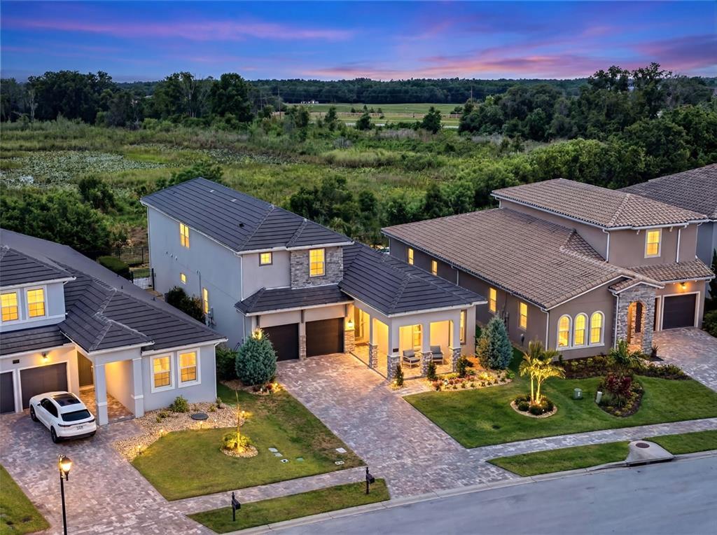 An aerial view shows three suburban houses with tiled roofs and paved driveways at dusk — 16049 VOLTERRA POINT, MONTVERDE, FL