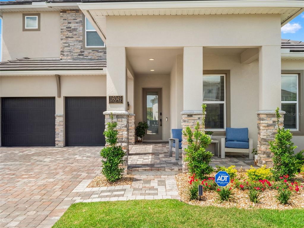 The exterior of a two-story house features a stone-accented porch, garage, and paved driveway — 16049 VOLTERRA POINT, MONTVERDE, FL