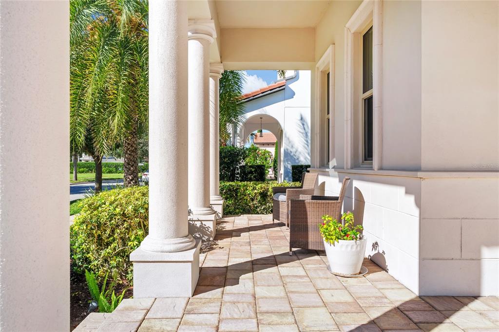 A covered porch features stone pavers, white columns, and wicker chairs beside a potted plant — 15625 SYLVESTER PALM DRIVE, WINTER GARDEN, FL