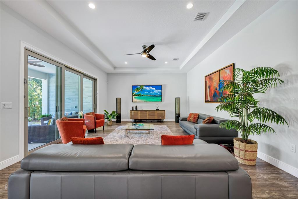 A living room features a gray sectional, orange armchairs, a television, and a sliding glass door — 15625 SYLVESTER PALM DRIVE, WINTER GARDEN, FL