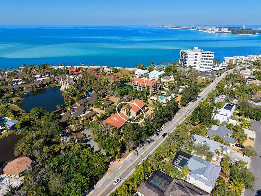 An aerial view shows a multi-story residential building circled in a lush, coastal neighborhood — 117 PASS KEY ROAD UNIT 117, SARASOTA, FL