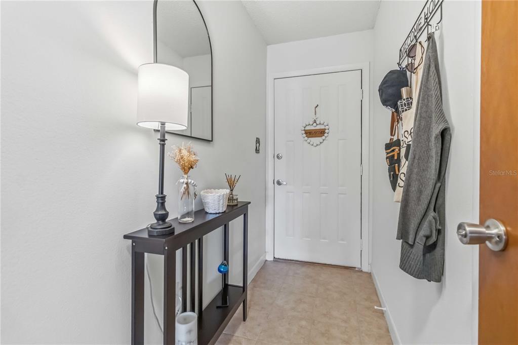 A narrow entryway features a dark console table, a lamp, a mirror, and a door — 1675 S FISKE BOULEVARD UNIT G227, ROCKLEDGE, FL