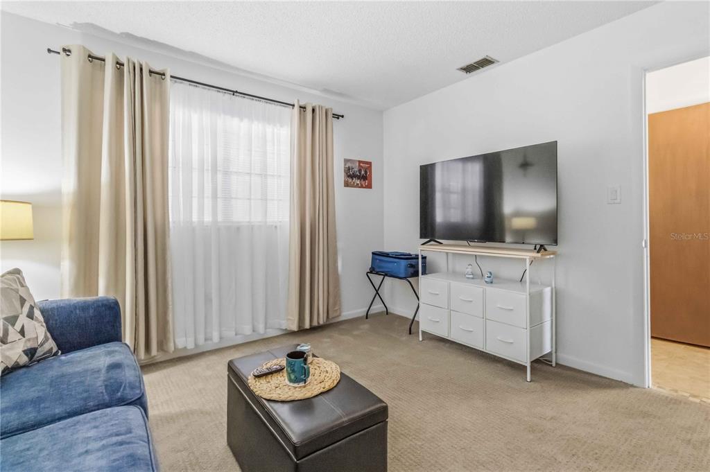 A living room features a blue sofa, a television on a white dresser, and beige curtains — 1675 S FISKE BOULEVARD UNIT G227, ROCKLEDGE, FL