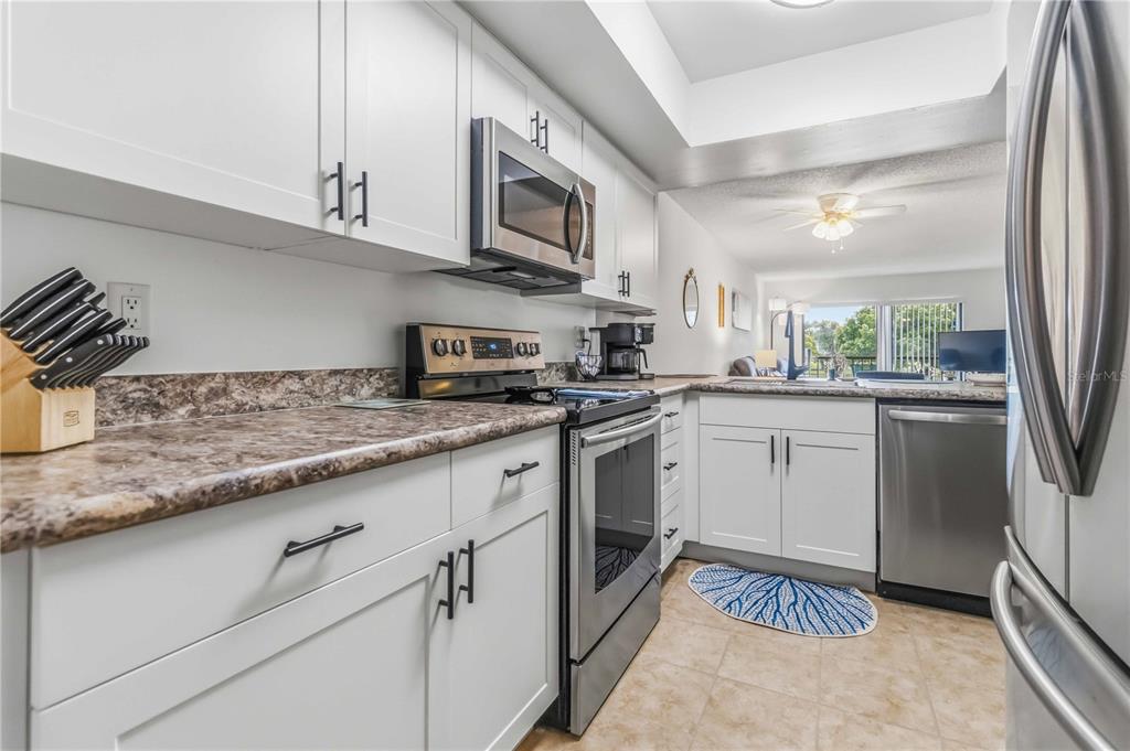 A galley-style kitchen features white cabinets, stainless steel appliances, and brown laminate countertops — 1675 S FISKE BOULEVARD UNIT G227, ROCKLEDGE, FL