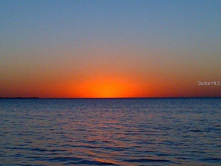 A vibrant orange sunset glows over a calm body of water at the horizon — 5141 WESTSHORE DRIVE, NEW PORT RICHEY, FL