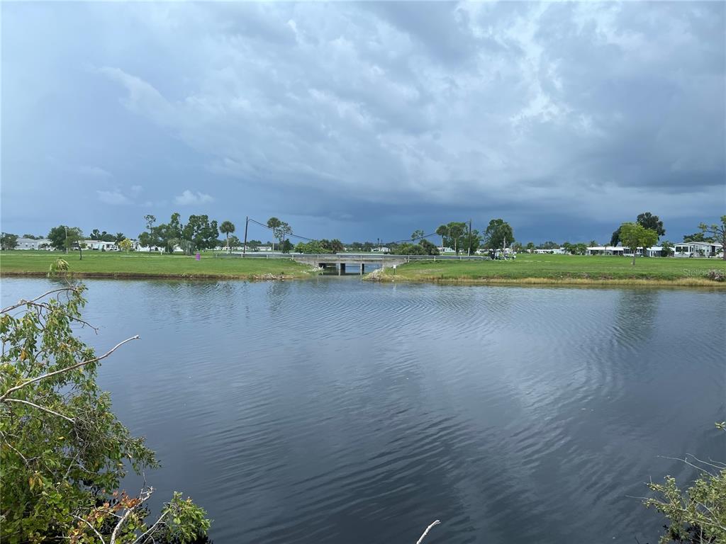 A view of a calm pond with a small concrete bridge and grassy landscape beyond — 14206 OSTROM AVENUE, PORT CHARLOTTE, FL