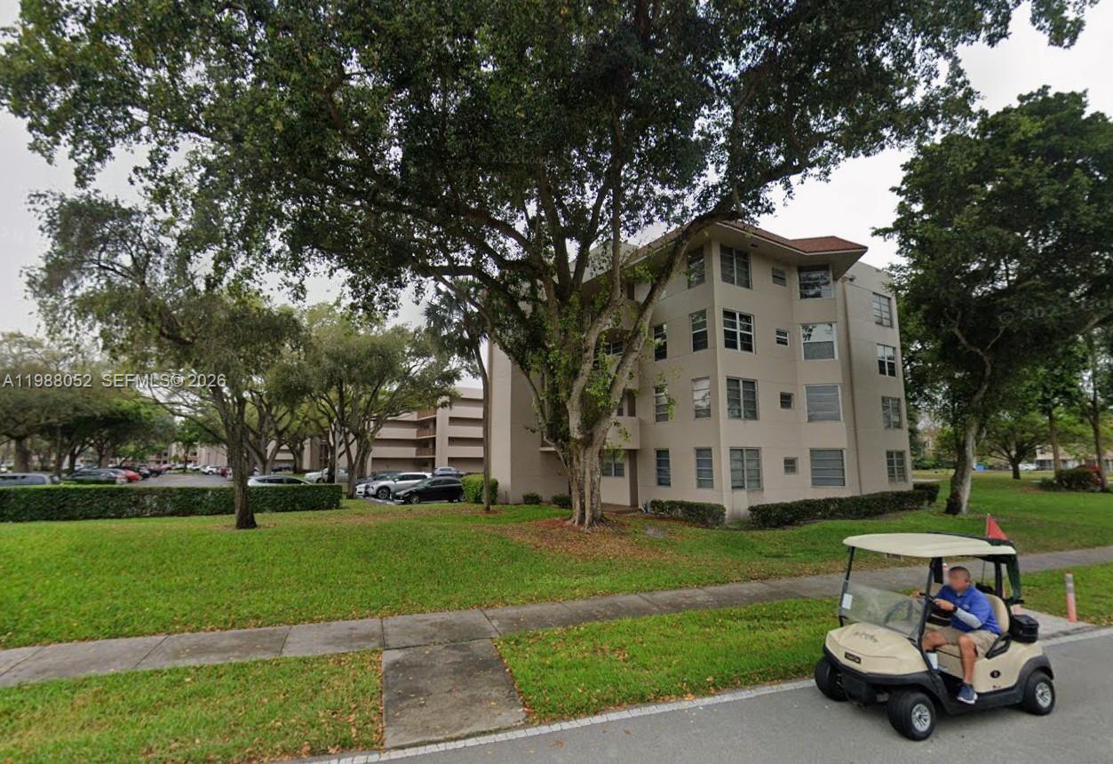 A multi-story apartment building stands behind a grassy lawn with a golf cart in front — 1811 Sabal Palm Dr # 408, Davie FL 33324, DAVIE, FL
