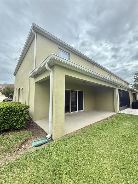 A covered concrete patio extends from the rear of a two-story tan stucco house — 403 ARBOR LAKES DRIVE, DAVENPORT, FL