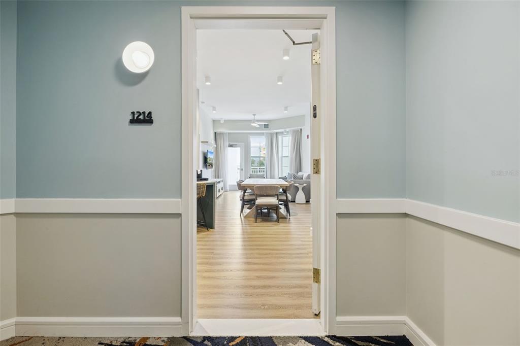 A view through an open doorway reveals a modern apartment interior with light wood flooring — 3151 SUNSET WALK DRIVE UNIT 1214, KISSIMMEE, FL