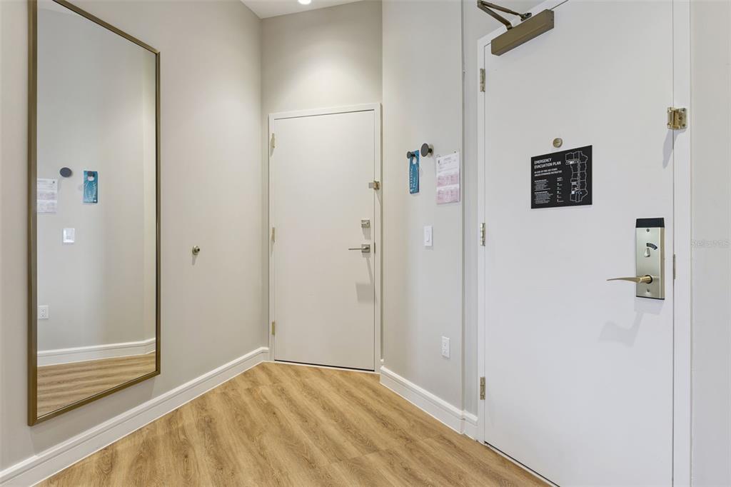 An entryway features light wood-look flooring, a large wall mirror, and two white doors — 3151 SUNSET WALK DRIVE UNIT 1214, KISSIMMEE, FL