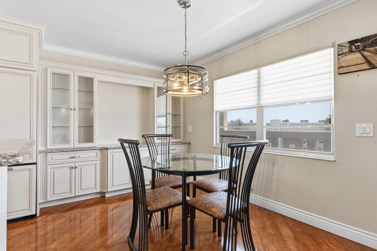 A dining area features a glass table, four chairs, built-in cabinetry, and hardwood flooring — 4037 Ainslie C, Boca Raton FL 33434, BOCA RATON, FL
