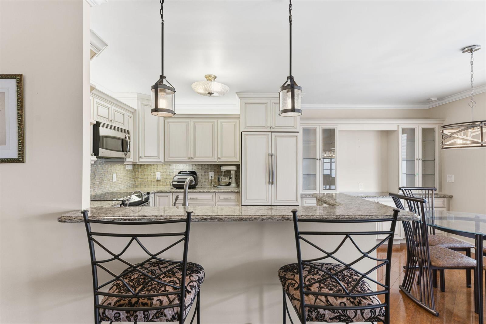 A kitchen features cream-colored cabinetry, granite countertops, a breakfast bar, and two pendant lights — 4037 Ainslie C, Boca Raton FL 33434, BOCA RATON, FL