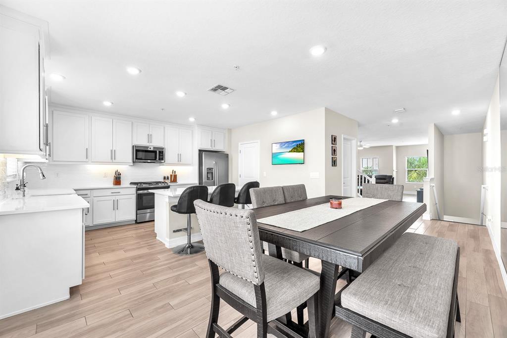 A modern kitchen and dining area featuring white cabinets, stainless appliances, and light wood flooring — 5351 BRIDGE STREET UNIT 16, TAMPA, FL