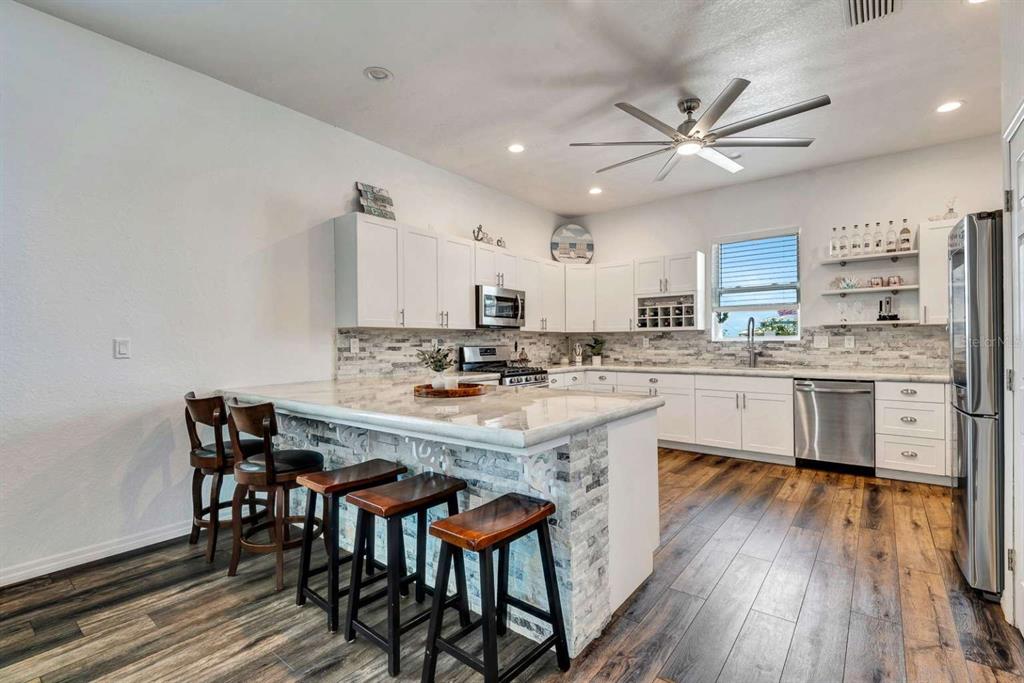 A kitchen with white cabinets, stone backsplash, a breakfast bar with stools, and wood flooring — 217 22ND STREET COURT NE, BRADENTON, FL