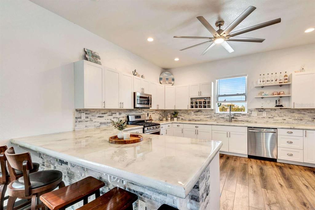 A kitchen features white cabinets, a stone backsplash, a marble-topped island, and wood-look flooring — 217 22ND STREET COURT NE, BRADENTON, FL