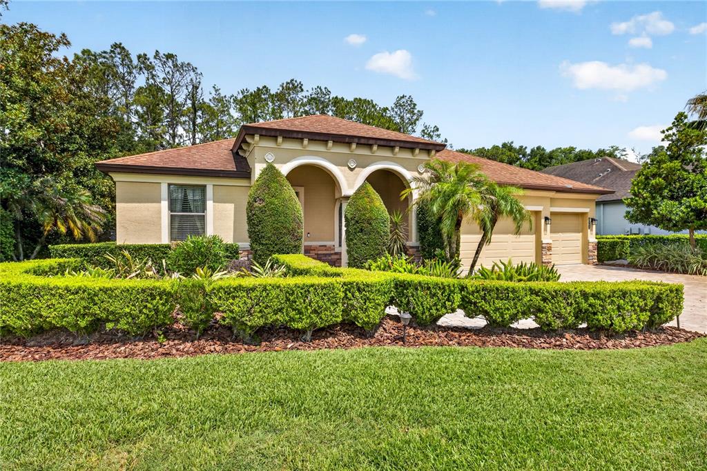A single-story house with a tan stucco exterior, arched entryway, and manicured hedges — 4726 LAGO VISTA CIRCLE, LAND O LAKES, FL