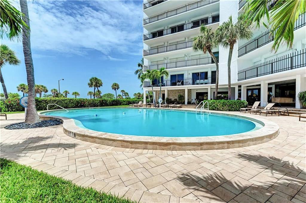 A swimming pool sits on a paved patio in front of a multi-story apartment building — 1 BENJAMIN FRANKLIN DRIVE UNIT 3, SARASOTA, FL