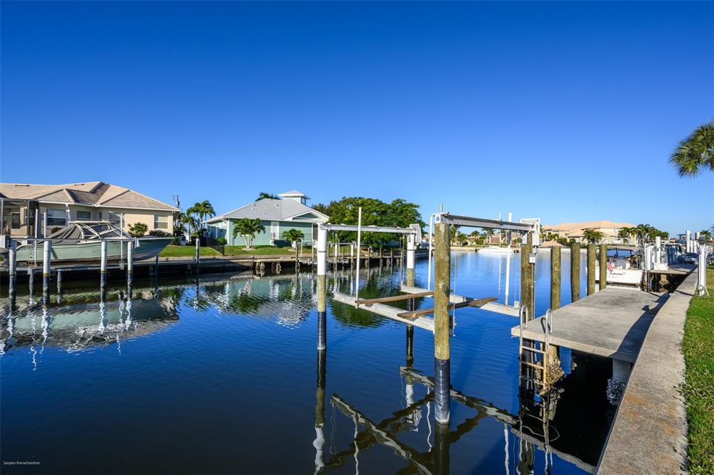A canal view showing a boat lift, a concrete dock, and residential houses under a sky — 149 CRESCENT DRIVE, PUNTA GORDA, FL