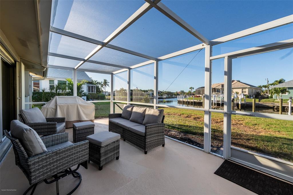 A screened-in patio with outdoor furniture overlooks a canal and neighboring houses — 149 CRESCENT DRIVE, PUNTA GORDA, FL
