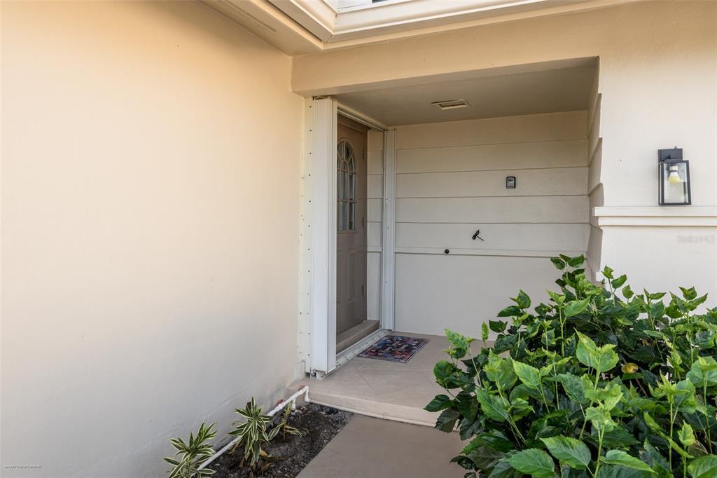 A covered entryway features a brown front door, light-colored siding, and a small garden bed — 149 CRESCENT DRIVE, PUNTA GORDA, FL