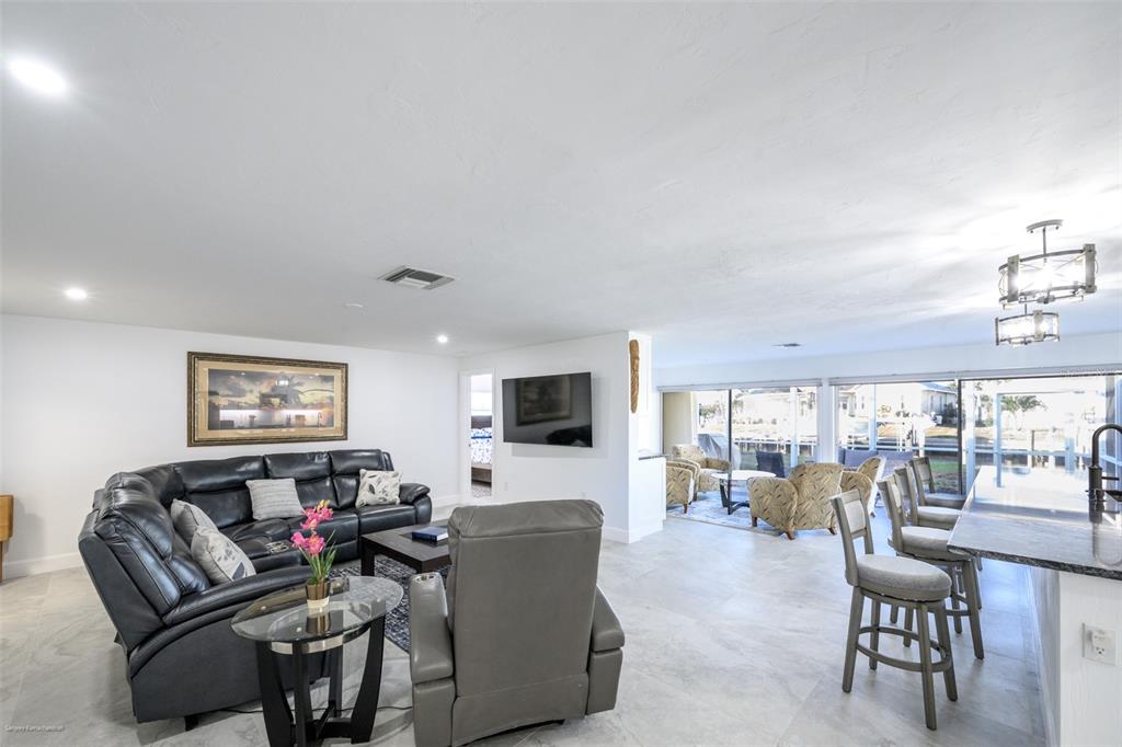 An open-concept living room features a black leather sectional, gray recliner, and kitchen island seating — 149 CRESCENT DRIVE, PUNTA GORDA, FL